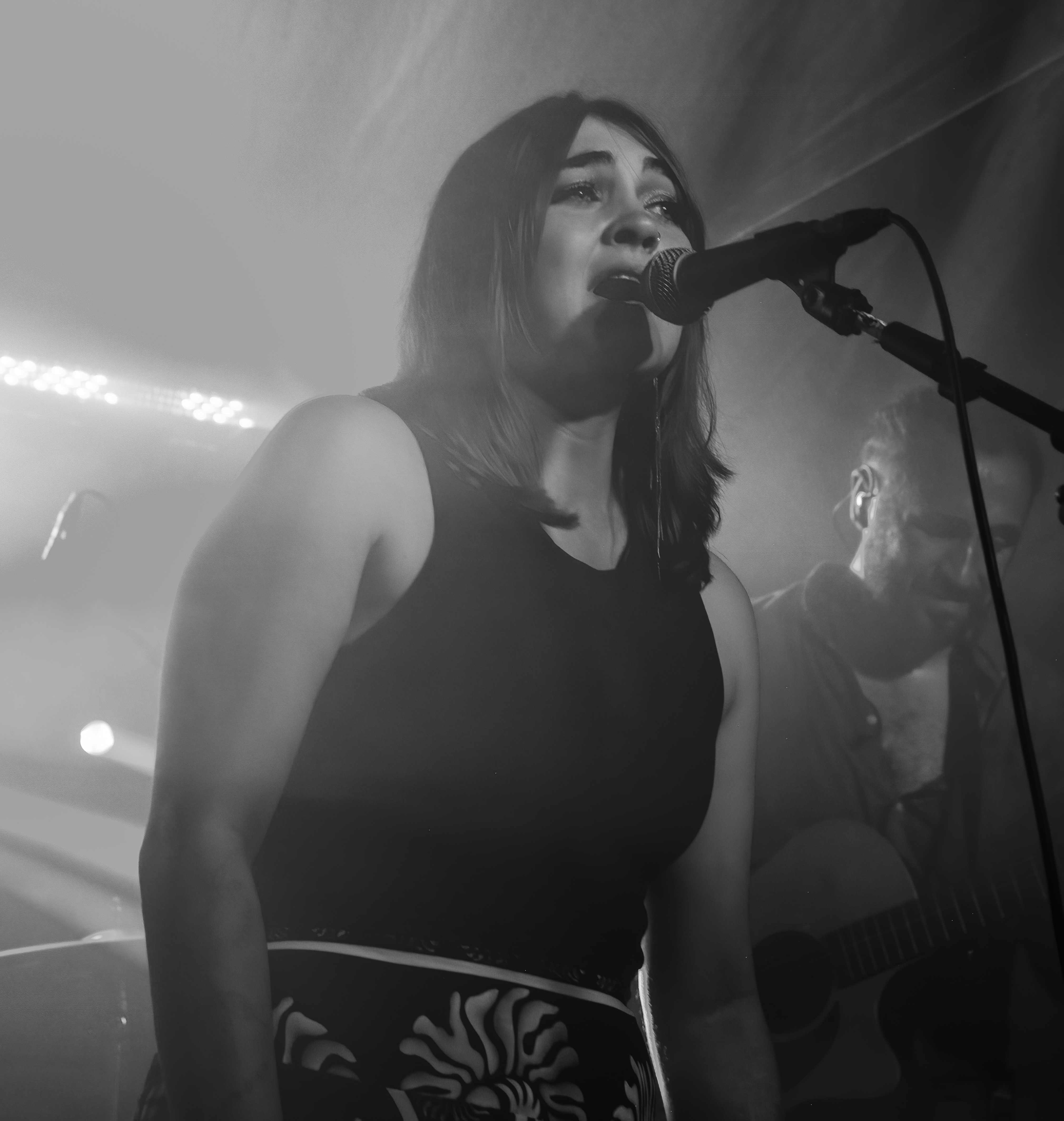 A female singer passionately performing on stage, with a microphone in hand and dramatic lighting creating a smoky atmosphere.